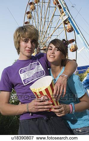 Stock Photo - Teenage couple in front of Ferris wheel in amusement park. Fotosearch