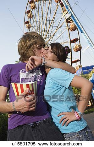 Stock Photography - Teenage couple in front of Ferris wheel in amusement park. Fotosearch