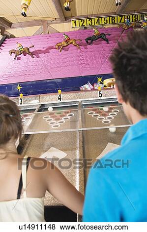 Teenage couple playing horse racing game in amusement park View Large Photo Image Stock Photo - Teenage couple playing horse racing game in amusement park. Fotosearch