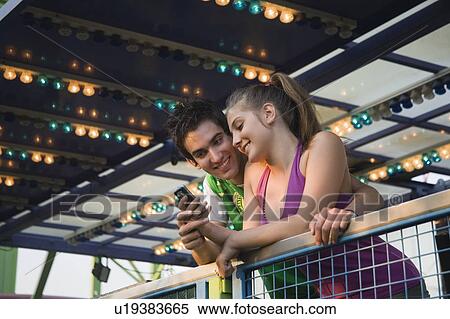 Teenage couple with cell phone at amusement park ride View Large Photo Image Stock Photography - Teenage couple with cell phone at amusement park ride. Fotosearch