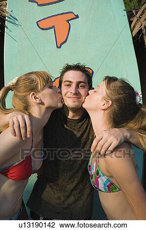 Stock Image - Two female teenagers kissing male teenager on cheek. Fotosearch