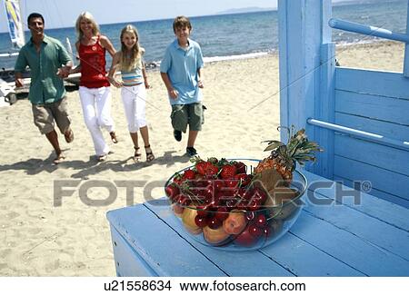 Picture - Bowl of fruit and parents with children on beach. Fotosearch