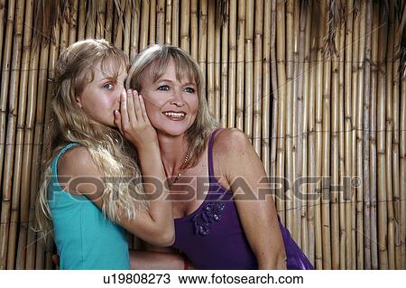 Stock Image - Daughter whispering in mother's ear. Fotosearch