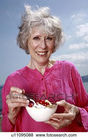 Female senior eating yogurt and fruit on the beach View Large Photo Image Stock Photo - Female senior eating yogurt and fruit on the beach. Fotosearch