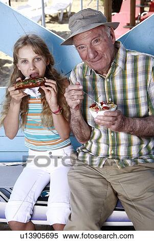 Stock Photography - Grandfather and granddaughter eating at beach. Fotosearch