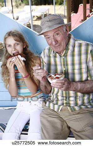 Stock Photography - Grandfather and granddaughter eating at beach. Fotosearch