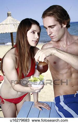 Stock Image - Young adult couple eating breakfast on beach. Fotosearch