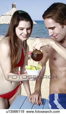 Stock Photo - Young adult couple eating breakfast on beach. Fotosearch