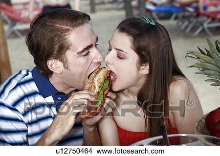 Picture - Young adult couple eating sandwich. Fotosearch