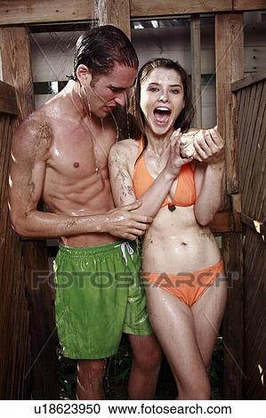 Stock Image - Young adult couple taking shower in bathing suits. Fotosearch