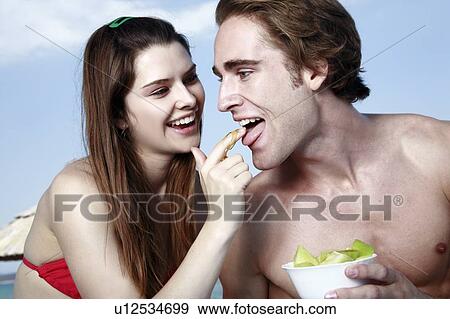 Stock Photo - Young man eating honey from young woman's finger. Fotosearch