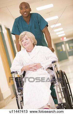 Stock Image - An Orderly Pushing A Senior Woman In A Wheelchair Down A Hospital Corridor. Fotosearch