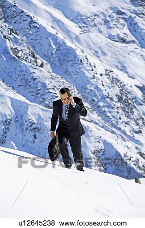 Businessman outdoors on snowy mountain using cellular phone View Large Photo Image Stock Photo - Businessman outdoors on snowy mountain using cellular phone. Fotosearch