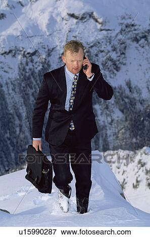 Stock Photo - Businessman outdoors on snowy mountain using cellular phone. Fotosearch
