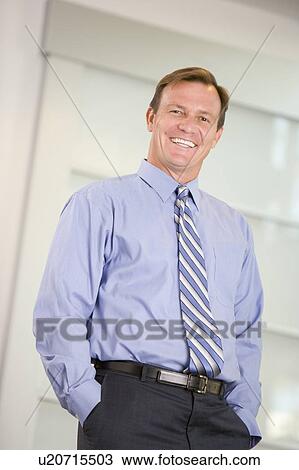 Businessman standing indoors smiling View Large Photo Image Stock Image - Businessman standing indoors smiling. Fotosearch