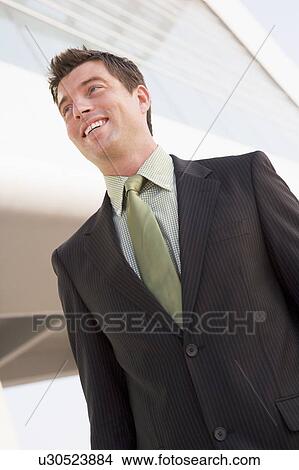 Picture - Businessman standing outdoors by building smiling. Fotosearch