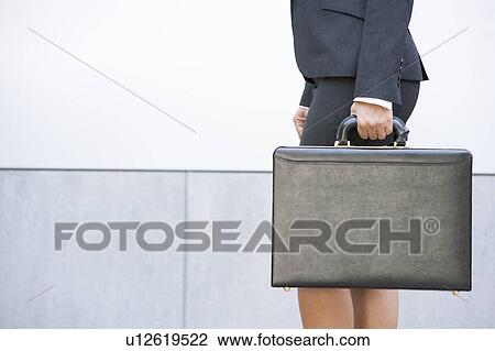 Stock Image - Businesswoman holding briefcase outdoors. Fotosearch