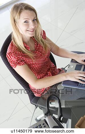 Stock Photo - Businesswoman sitting in office typing on laptop smiling. Fotosearch
