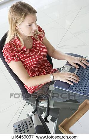 Stock Photo - Businesswoman sitting in office typing on laptop. Fotosearch