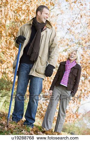 Stock Photo - Couple outdoors raking leaves and smiling (selective focus). Fotosearch