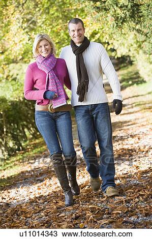 Stock Image - Couple outdoors walking on path in park smiling (selective focus). Fotosearch