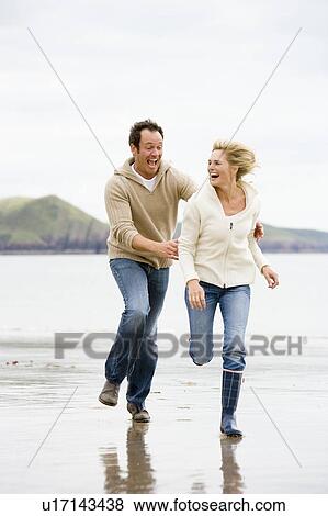 Stock Photo - Couple running on beach smiling. Fotosearch