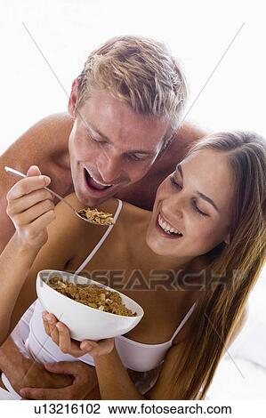 Couple sitting in bedroom eating cereal and smiling View Large Photo Image Stock Image - Couple sitting in bedroom eating cereal and smiling. Fotosearch