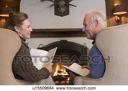 Couple sitting in living room by fireplace with books smiling View Large Photo Image Picture - Couple sitting in living room by fireplace with books smiling. Fotosearch