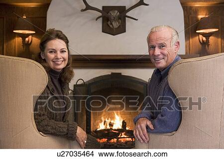 Couple sitting in living room by fireplace smiling View Large Photo Image Picture - Couple sitting in living room by fireplace smiling. Fotosearch