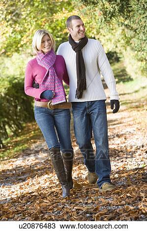 Stock Image - Couple walking outdoors on path in park smiling (selective focus). Fotosearch