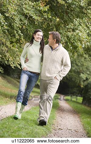 Stock Photography - Couple walking outdoors on path in park smiling (selective focus). Fotosearch