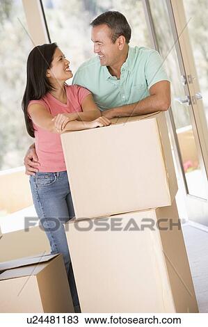 Stock Image - Couple with boxes in new home smiling. Fotosearch