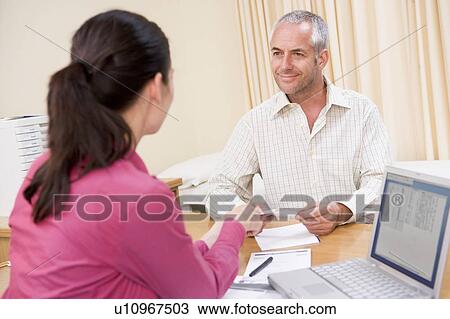Stock Image - Doctor with laptop and man in doctor's office smiling. Fotosearch