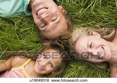Stock Photograph - Family lying in grass smiling. Fotosearch