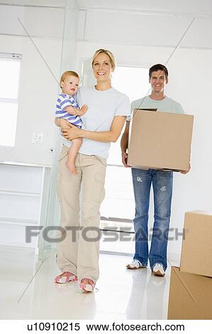 Stock Photography - Family with box moving into new home smiling. Fotosearch