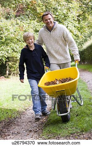 Stock Image - Father and son pushing wheelbarrow on path. Fotosearch