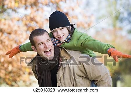 Father piggybacking son outdoors at park and smiling (selective focus) View Large Photo Image Stock Photo - Father piggybacking son outdoors at park and smiling (selective focus). Fotosearch
