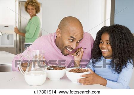 Father Sitting With Daughter As She They Eat Breakfast With Her Mother In The Background View Large Photo Image Picture - Father Sitting With Daughter As She They Eat Breakfast With Her Mother In The Background . Fotosearch