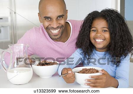 Stock Photo - Father Sitting With Daughter As She They Eat Breakfast. Fotosearch