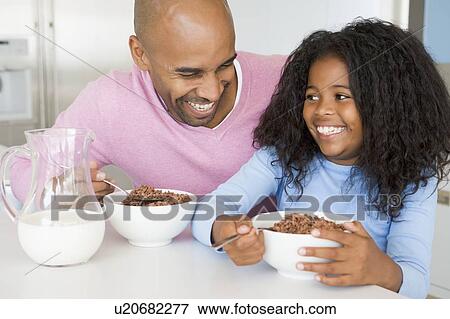 Stock Photo - Father Sitting With Daughter As She They Eat Breakfast. Fotosearch