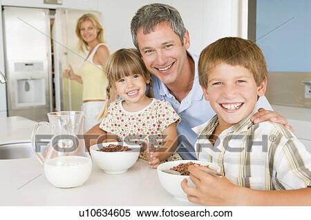 Stock Photography - Father With Children As They Eat Breakfast And Mother In The Back Ground . Fotosearch