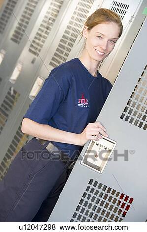 Stock Photo - Firewoman holding her locker door open in fire station locker room (depth of field). Fotosearch