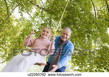 Grandfather outdoors pushing granddaughter on swing and smiling (selective focus) View Large Photo Image Stock Image - Grandfather outdoors pushing granddaughter on swing and smiling (selective focus). Fotosearch