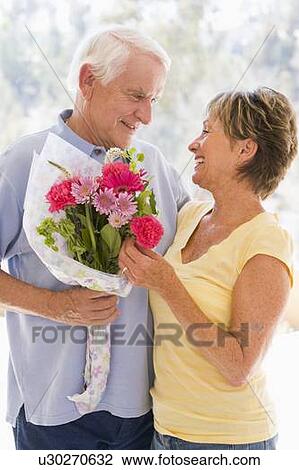 Stock Image - Husband giving wife flowers and smiling. Fotosearch