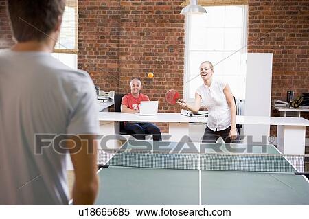 Stock Photography - Man and woman in office space playing ping pong. Fotosearch