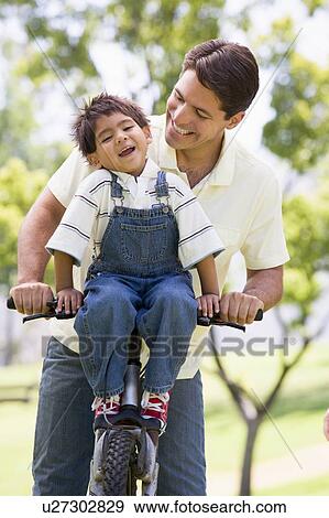 Stock Photo - Man and young boy on a bike outdoors smiling. Fotosearch