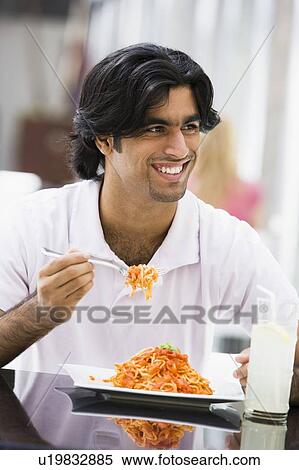 Stock Photography - Man at restaurant eating spaghetti and smiling (selective focus). Fotosearch