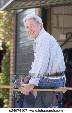 Stock Photo - Man at shed sitting on tool bench smiling. Fotosearch