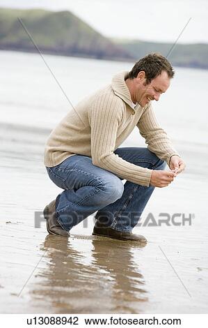 Man crouching on beach smiling View Large Photo Image Stock Image - Man crouching on beach smiling. Fotosearch