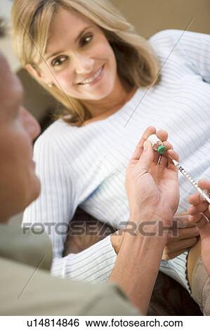 Stock Photograph - Man helping woman inject drugs to prepare for IVF treatment (selective focus). Fotosearch